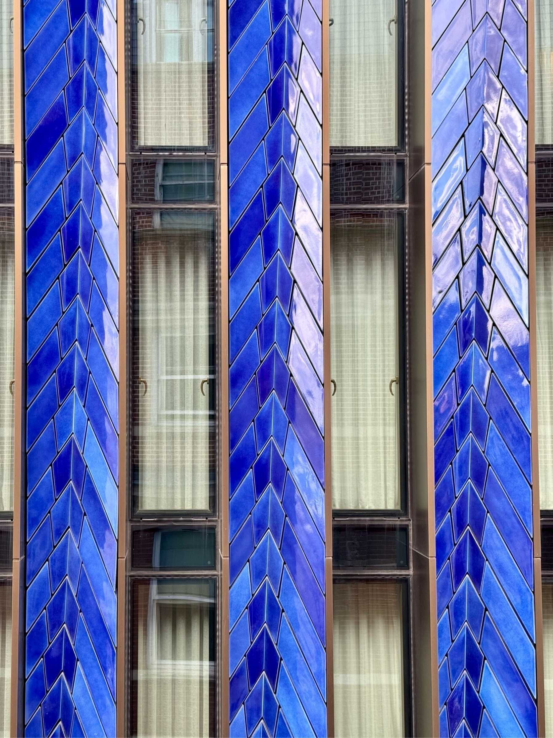 Close of of the side of a building with shiny blue dragon skin-like tiles between columns of windows